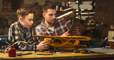 Father and son are modeling a toy airplane in a garage at home.