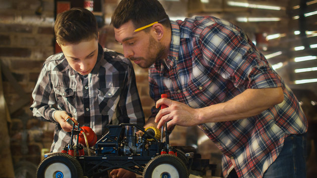 Father And Son Are Working On A Radio Control Toy Car In A Garage At Home.