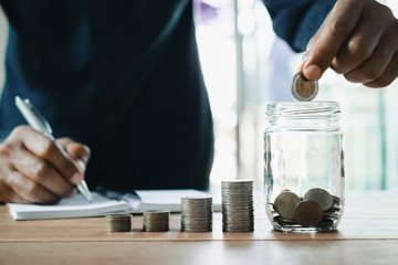 Men are Saint documents about save money and put coin in glass jar on desk.