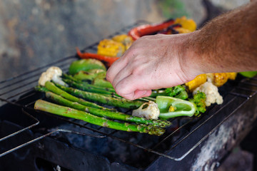 A man grills corn, pepper and asparagus. Concept - healthy eating in the family, vegetarianism, men's hobby.
