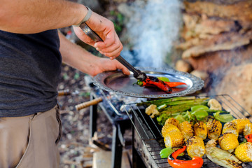 A man grills corn, pepper and asparagus. Concept - healthy food in the family, male hobby, a man prepares food.