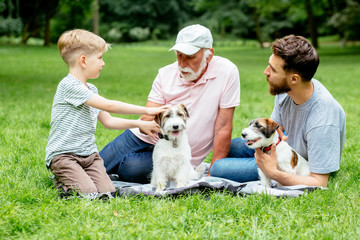 Grandfather, father and son and two dogs Jack russel terrier lying on the green grass in the summer park. Family Vacation. Generational connection. family, pet, love friendship and people concept