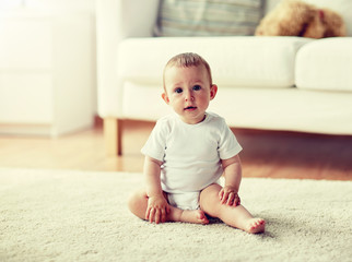 childhood, babyhood and people concept - happy little baby boy or girl sitting on floor at home