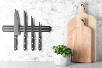 Magnetic holder with set of knives on marble wall in kitchen