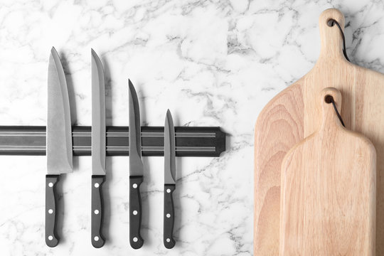 Magnetic holder with set of knives and wooden boards against marble background