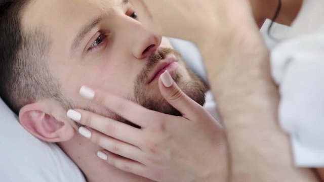 selective focus of handsome bearded man looking at woman, touching face and kissing in bedroom 