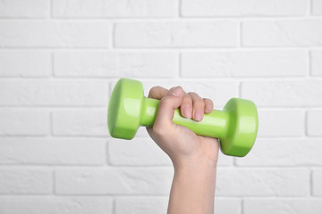 Woman holding dumbbell against brick wall, closeup. Home fitness