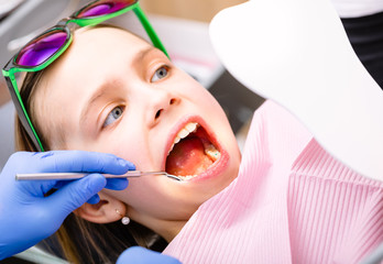 Preteen girl looking at her cured teeth in the mirror in pediatric dental clinic