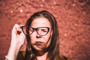 Young woman with short brown hair sitting in the bright sun while holding her eyeglasses – Girl focusing vision while looking through black reading glasses – Person with poor eyesight