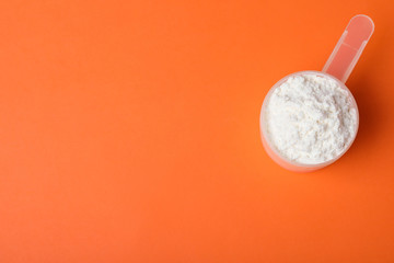 Scoop of protein powder on orange background, top view with space for text