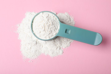 Scoop and pile of protein powder on pink background, flat lay