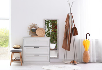 Modern hallway interior with chest of drawers and clothes on hanger stand. Space for text