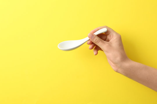 Woman holding empty miso soup spoon on color background, closeup. Space for text
