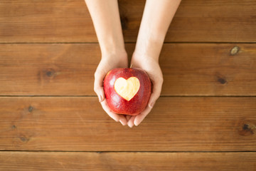 food, valentines day and health concept - close up of hands holding ripe red apple with carved...