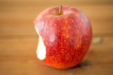 fruits, food and harvest concept - ripe red bitten apple on wooden table