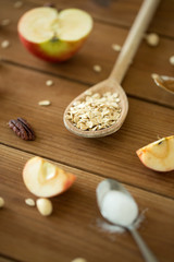 food cooking and eating concept - oatmeal in spoon, cut apples and nuts on wooden table