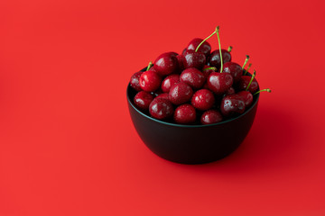 Freshly picked cherries in a black ceramic bowl. Bright red background, water drops, negative space, high resolution