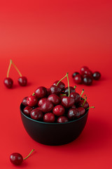 Freshly picked cherries in a black ceramic bowl. Bright red background, water drops, negative space, high resolution