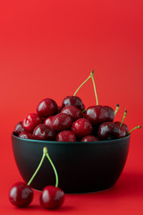 Freshly picked cherries in a black ceramic bowl. Bright red background, water drops, negative space, high resolution