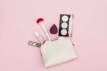 Eyeshadow palette; nail polish bottle; blender; makeup brush and makeup bag on pink background