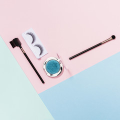 Makeup brushes; eyelashes and blue eyeshadow on pink; blue and light green backdrop