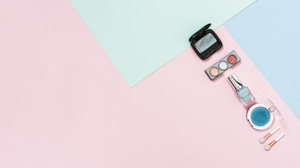 Eyeshadow palette; compact powder; nail polish bottle and brush on pastel background