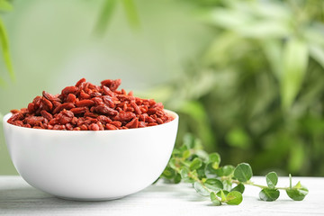 Bowl of dried goji berries on table against blurred background. Space for text