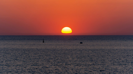 Red solar disk goes beyond the horizon at sunset