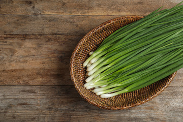 Wicker bowl with green onions on wooden table, top view Space for text