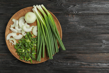 Wooden plate with cut onion leaves and bulbs on dark wooden table, top view. Space for text