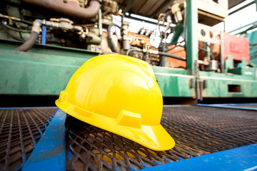 Yellow hardhat or safety helmet is placed on working platform of pumping unit in oil field operation. Selected focus on the hard hat. Safety, no accident in workplace concept - obrazy, fototapety, plakaty