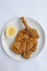 Succulent Traditional Italian Crummed and  Deep Fried Veal Cutlet or (Cotaletta alla Milanese) presented on an isolated white plate and white background with a slice of lemon