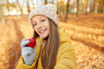 season and people concept - happy girl with apple taking selfie at autumn park