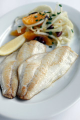 Grilled Fish Fillets with Fennel, Orange and Olive Salad isolated on a white plate and white background with a slice of lemon and chives
