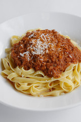Delicious Fresh Fettuccine Pasta with Bolognese sauce and sprinkled with Permesan Cheese isolated on white plate and white background