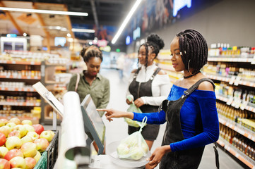 Group of african womans weighs apples in polyethylene bags at supermarket.