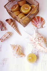 Still life: beeswax candles in a gold wire mesh box with sea shells on a white wooden table, top view