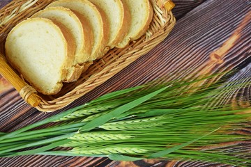 Fresh bread in a wicker basket and green ears on a wooden background.