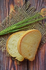 Fresh bread in a wicker basket and green ears on a wooden background.