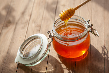 Pot Of Honey And Wooden Stick Are On A Table outdoors