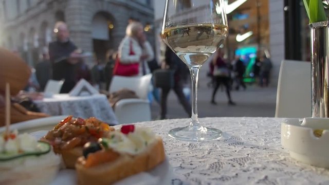 Close-up video with brusquest and glass of white wine. Restaurant. Out of focus people on the street in background.