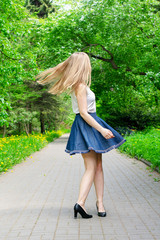 Young woman spinning in the park. The girl in the blue skirt is dancing on the street