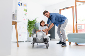 Father helping his son to drive a toy peddle car