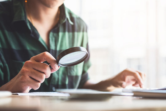 Man looking through a magnifying glass to documents. Business assessment and audit. Magnifying glass on a financial report. Close-up Of person Checking Bills With Magnifying Glass.Concept of search