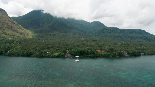 Aerial drone view of a cross and sunken cemetery with large volcanos behind (Camiguin, Philippines)