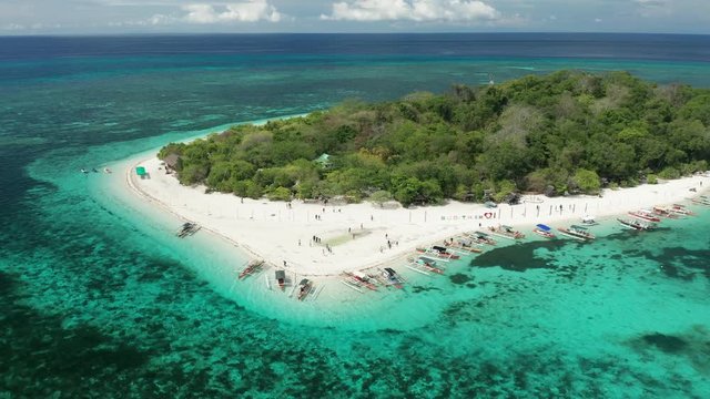 Aerial drone view of a tiny, beautiful tropical island with sandy beach, lush forest and coral reef (Mantigue Island, Camiguin)