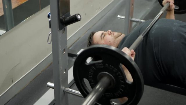 Young male performs a set of bench presses during a weight lifting session.