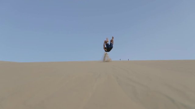 Young man having fun and doing a front flip on a sand dune