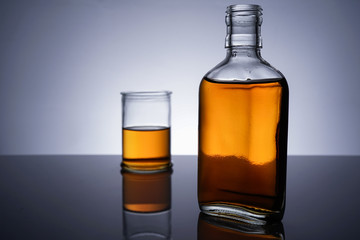 A backlit of a glass bottle and jar with golden liquid 