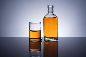 A backlit of a glass bottle and jar with golden liquid 